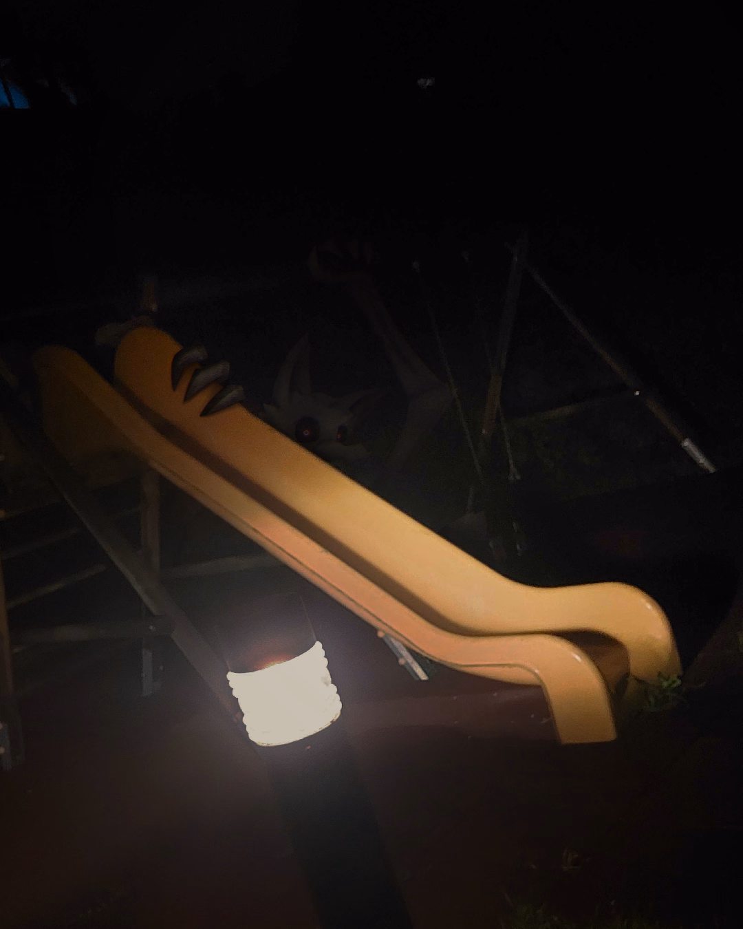 a creepy Edit of a photo on a playground, with a mysterious Monster looming in the shadows, drawn to look very realistic, to fit into the setting